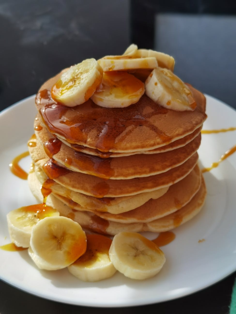 Stack of pancakes topped with banana slices and syrup